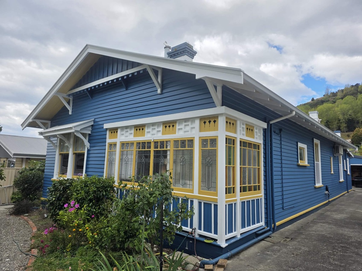 A blue weatherboard bungalow with white and yellow trim, seen from the corner