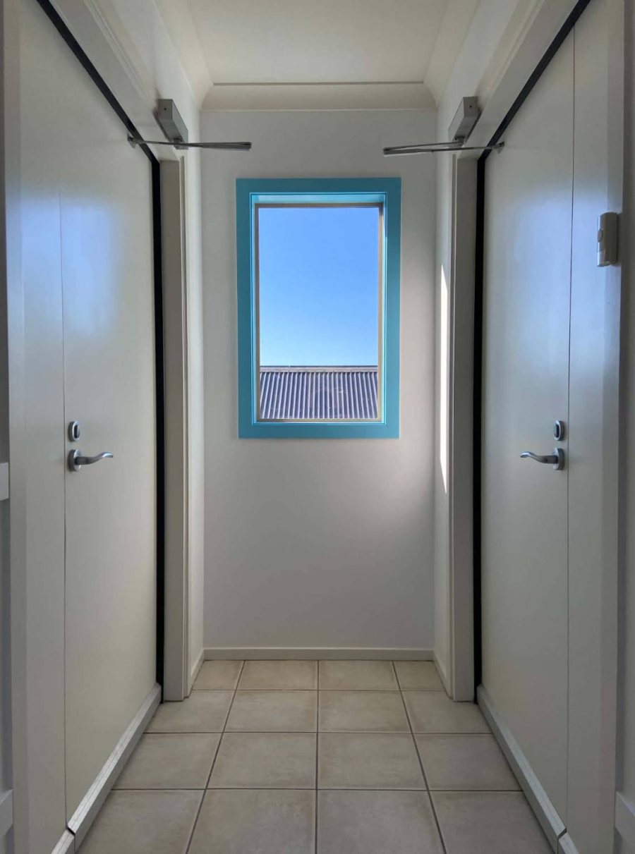 A freshly painted white hallway with a door on each side and a turquoise-framed window in the middle looking onto a blue sky